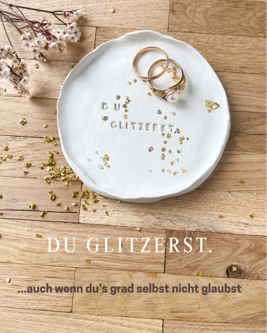 Schlichtes Geschirr mit Ringen darauf, umgeben von getrockneten Blumen und einer Botschaft.