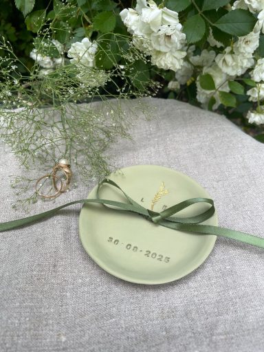 Kleiner, grüner Teller mit goldener Schrift und grünem Band, umgeben von Blumen.